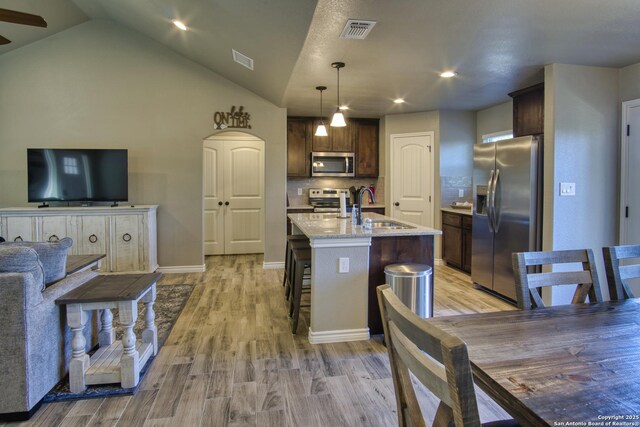 1139 Cedar Bnd, Canyon Lake, TX 78133 - kitchen with stainless steel appliances, a sink, dark brown cabinetry, light wood-style flooring, and a center island with sink