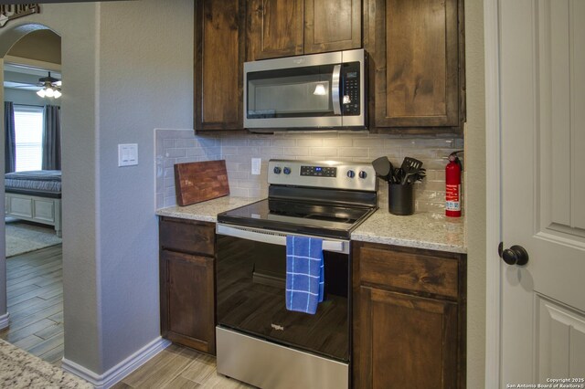 1139 Cedar Bnd, Canyon Lake, TX 78133 - kitchen featuring appliances with stainless steel finishes, tasteful backsplash, arched walkways, light wood-type flooring, and light stone counters