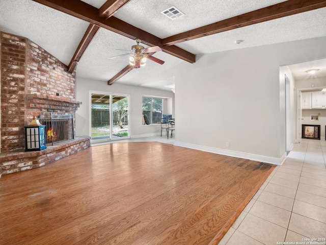 unfurnished living room featuring a brick fireplace, a textured ceiling, ceiling fan, tile patterned floors, and baseboards