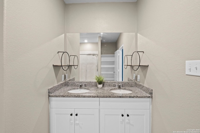 full bathroom with a textured wall, double vanity, and a shower stall