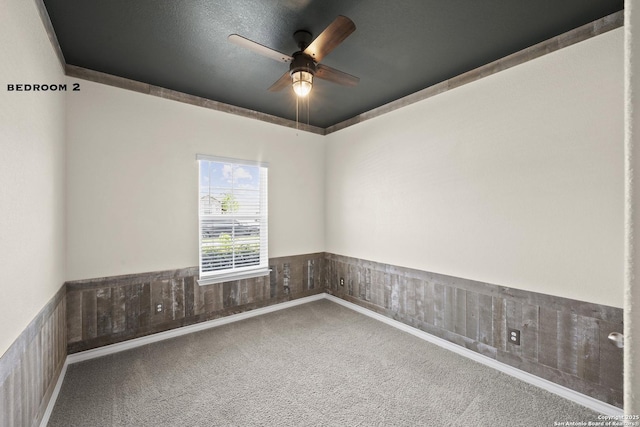 spare room with carpet floors, ceiling fan, and a wainscoted wall