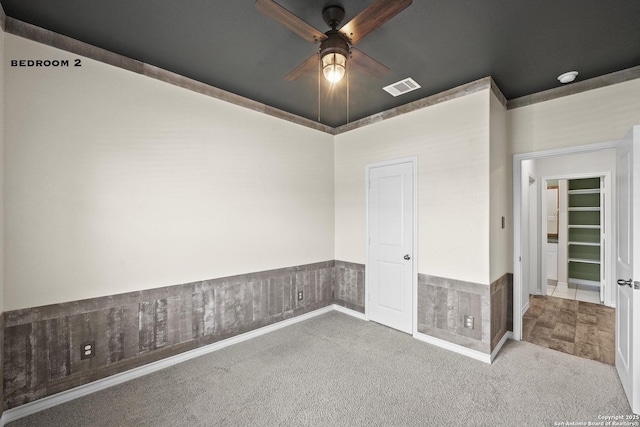 carpeted empty room featuring a ceiling fan and a wainscoted wall