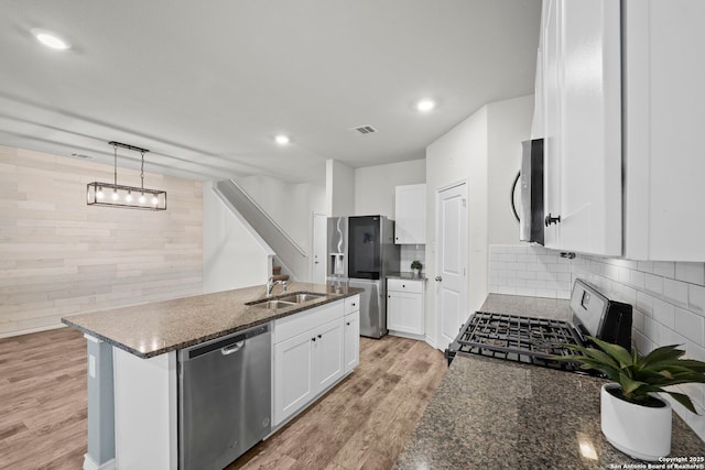 kitchen with stainless steel appliances, a sink, light wood-type flooring, dark stone countertops, and white cabinets
