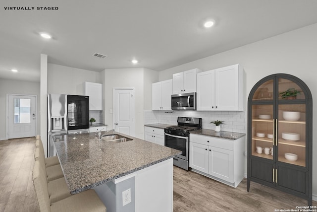 kitchen featuring stainless steel appliances, a sink, light wood-style floors, a kitchen island with sink, and dark stone counters