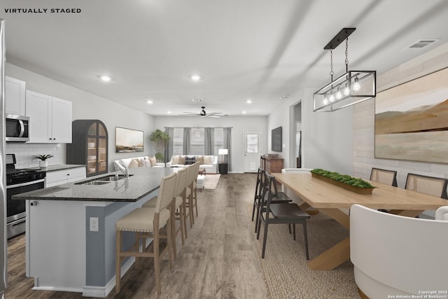 kitchen featuring appliances with stainless steel finishes, a kitchen breakfast bar, recessed lighting, a kitchen island with sink, and white cabinets