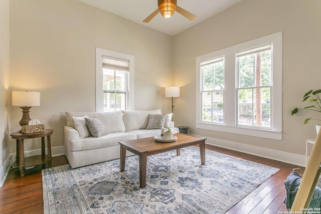 living room with dark wood-type flooring, a ceiling fan, and baseboards