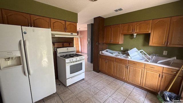 1906 Perlita, San Antonio, TX 78224 - kitchen with white appliances, under cabinet range hood, brown cabinets, light countertops, and light tile patterned floors