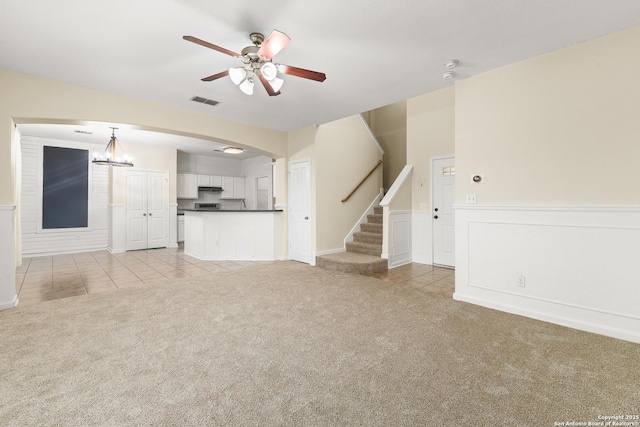 6739 Nora Vista Way, San Antonio, TX 78233 - unfurnished living room featuring light colored carpet, ceiling fan, stairway, light tile patterned floors, and a wainscoted wall