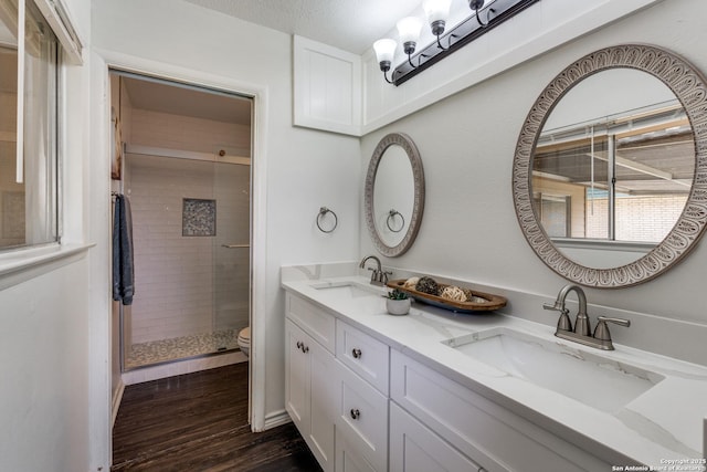 bathroom featuring a stall shower, wood finished floors, toilet, and double vanity