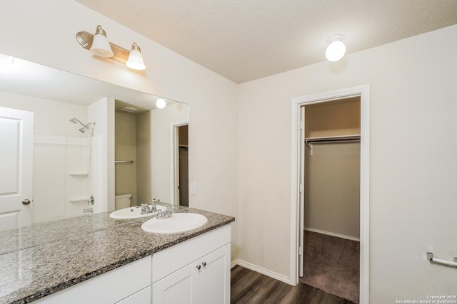 bathroom featuring wood finished floors, a walk in closet, a shower, and vanity