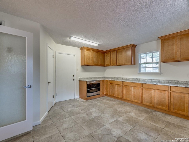 12802 Country Crst, San Antonio, TX 78216 - kitchen featuring stainless steel oven, brown cabinetry, light countertops, and a textured ceiling