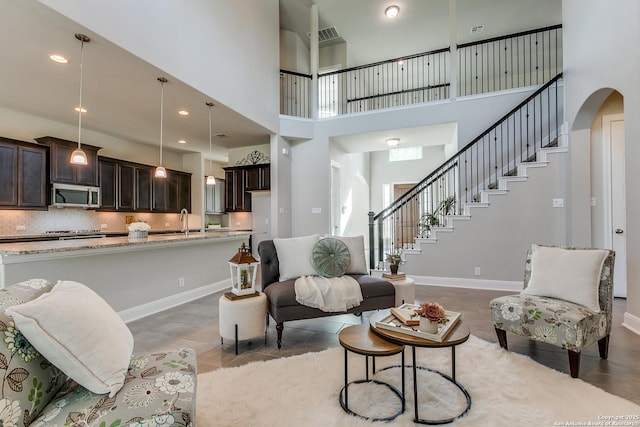 living area featuring arched walkways, a towering ceiling, stairs, baseboards, and recessed lighting