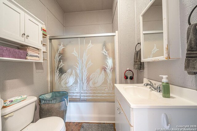 1004 Leona, Cotulla, TX 78014 - bathroom featuring a textured wall, toilet, vanity, bath / shower combo with glass door, and wood finished floors
