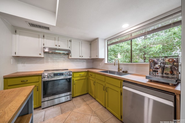 kitchen featuring stainless steel appliances, wooden counters, a sink, under cabinet range hood, and green cabinets