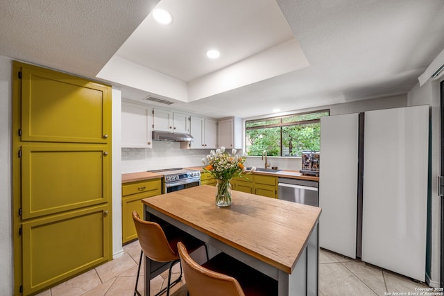 kitchen with a sink, stainless steel appliances, green cabinets, light tile patterned floors, and under cabinet range hood