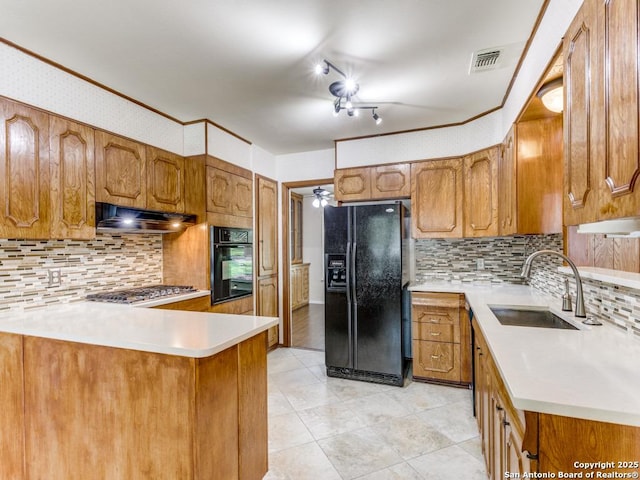 kitchen with black appliances, under cabinet range hood, a sink, and brown cabinets