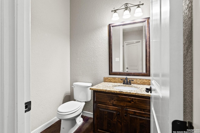 105 Saddle Up, La Vernia, TX 78121 - half bath featuring baseboards, toilet, vanity, a textured wall, and wood finished floors