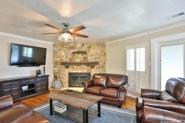 living area featuring ornamental molding, a ceiling fan, wood finished floors, a textured ceiling, and a stone fireplace