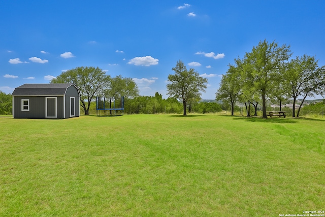 view of green lawn featuring a trampoline, a storage shed, and an outdoor structure