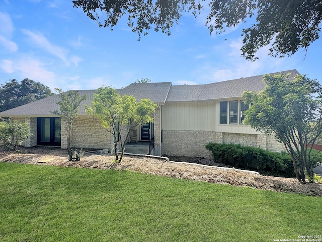 view of front of house with a front yard, roof with shingles, and stone siding
