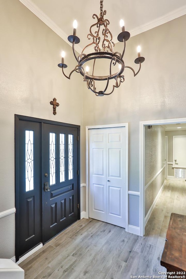 entryway featuring a chandelier, wood finished floors, crown molding, a towering ceiling, and baseboards