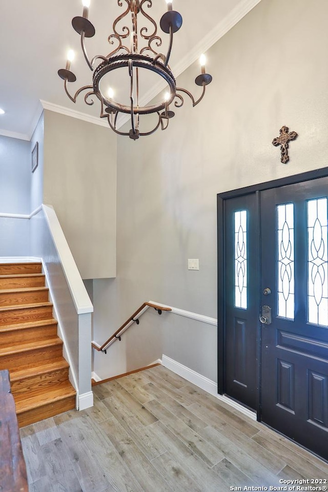 entrance foyer with a chandelier, crown molding, wood finished floors, and baseboards