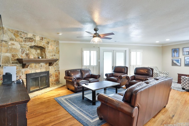 living area featuring ornamental molding, light wood-type flooring, a ceiling fan, a textured ceiling, and a stone fireplace