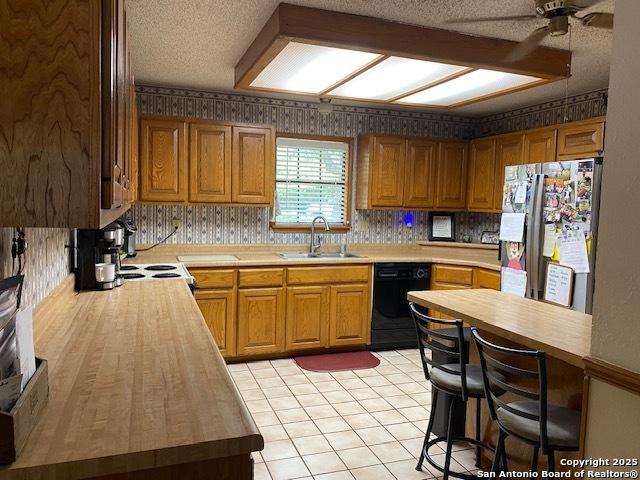 9516 Geronimo Oaks, San Antonio, TX 78254 - kitchen with a sink, freestanding refrigerator, dishwasher, wallpapered walls, and ceiling fan