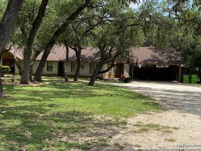 9516 Geronimo Oaks, San Antonio, TX 78254 - view of property hidden behind natural elements featuring dirt driveway, a front yard, and a carport