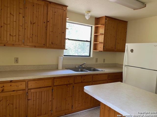 9516 Geronimo Oaks, San Antonio, TX 78254 - kitchen featuring freestanding refrigerator, a sink, brown cabinetry, light countertops, and open shelves