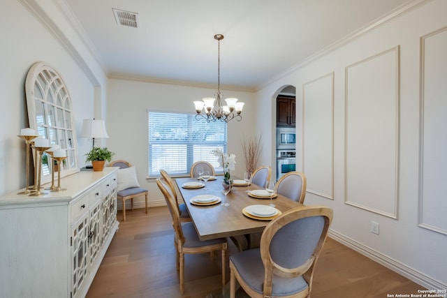 dining area with arched walkways, wood finished floors, baseboards, ornamental molding, and a chandelier