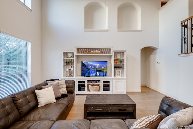 living area with a towering ceiling, arched walkways, and wood finished floors
