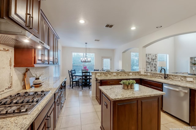 kitchen with stainless steel appliances, a sink, arched walkways, backsplash, and a center island