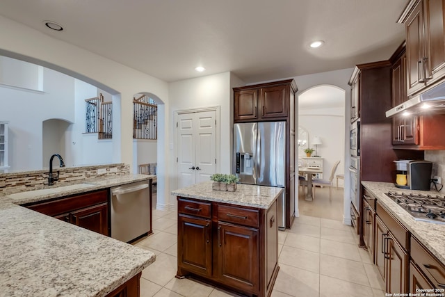 kitchen with stainless steel appliances, arched walkways, a sink, light tile patterned flooring, and backsplash