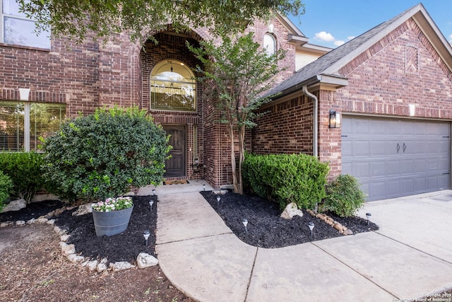 doorway to property with brick siding, an attached garage, and driveway