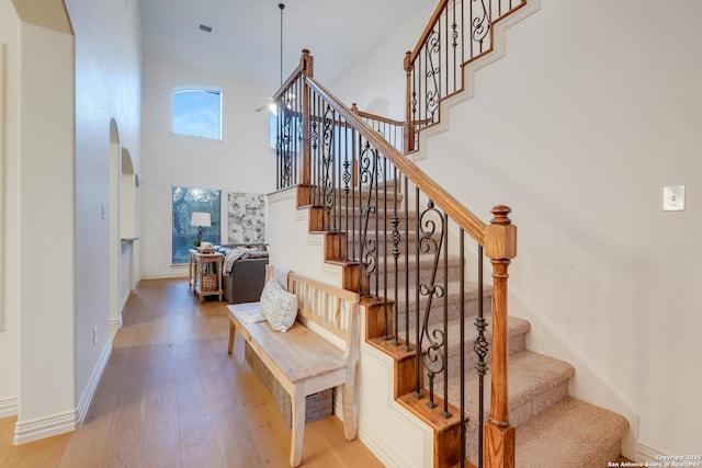 staircase featuring wood finished floors, arched walkways, a towering ceiling, and baseboards