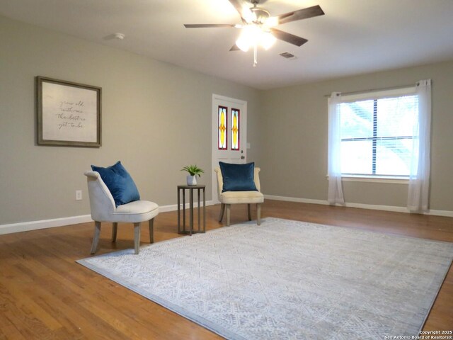 living area with a ceiling fan, wood finished floors, and baseboards