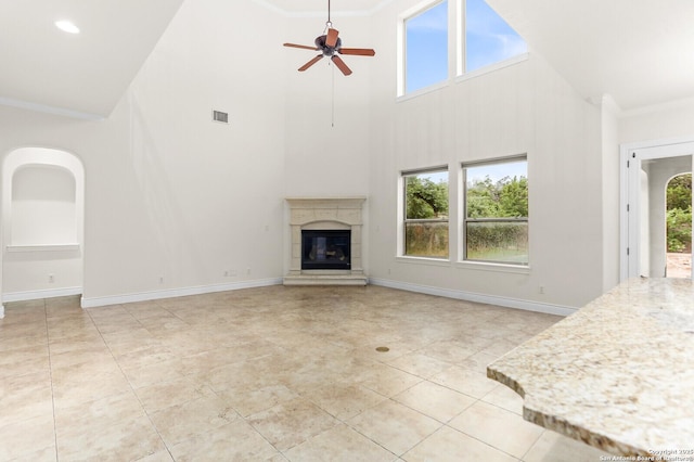 unfurnished living room with a high ceiling, a ceiling fan, a high end fireplace, crown molding, and light tile patterned flooring