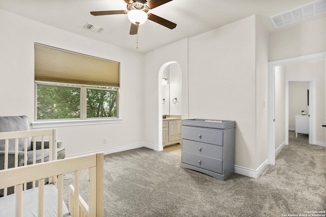 unfurnished bedroom with carpet floors, baseboards, arched walkways, ensuite bathroom, and a ceiling fan