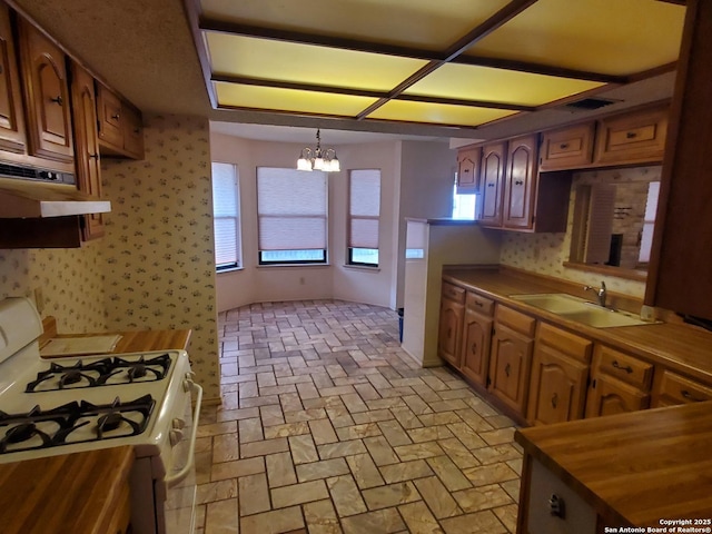 kitchen with white gas range, a sink, a chandelier, under cabinet range hood, and butcher block counters