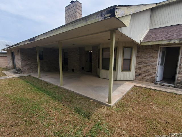 back of house featuring brick siding, a lawn, and a patio area