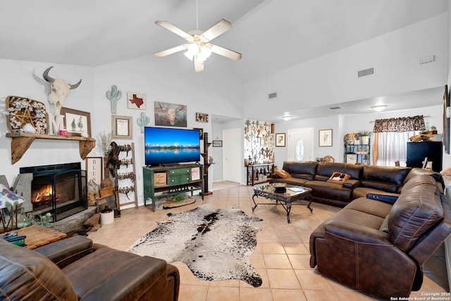 living room with light tile patterned floors, a ceiling fan, high vaulted ceiling, and a warm lit fireplace