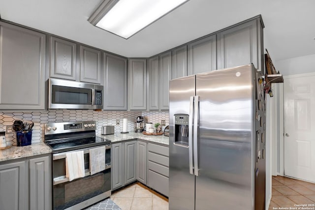 kitchen with gray cabinets, appliances with stainless steel finishes, light tile patterned flooring, and tasteful backsplash