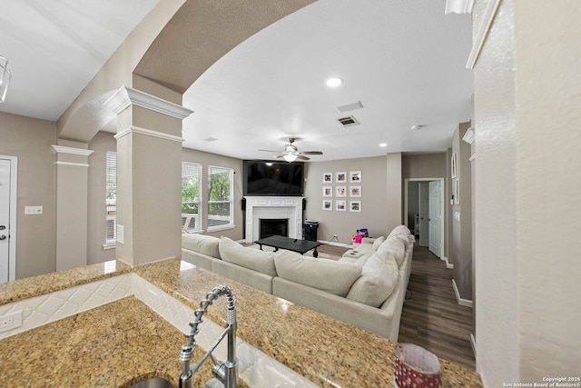 living room featuring a ceiling fan, a fireplace, ornate columns, wood finished floors, and recessed lighting