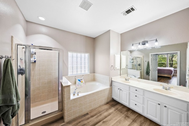 full bathroom featuring wood finished floors, a stall shower, a garden tub, double vanity, and ensuite bath