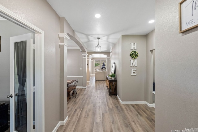 corridor featuring arched walkways, decorative columns, light wood-type flooring, baseboards, and recessed lighting