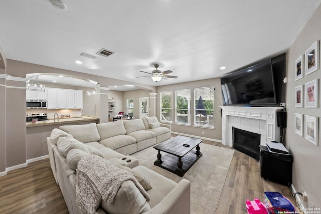 living area featuring ornate columns, wood finished floors, arched walkways, a tiled fireplace, and recessed lighting