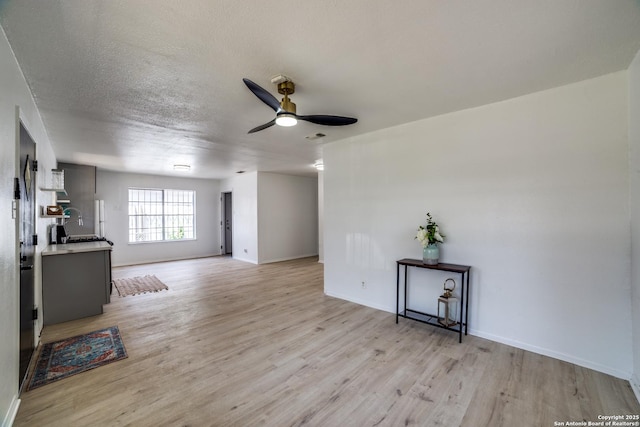 2114 S Trinity St, San Antonio, TX 78207 - unfurnished living room featuring light wood-style flooring, a ceiling fan, baseboards, and a textured ceiling