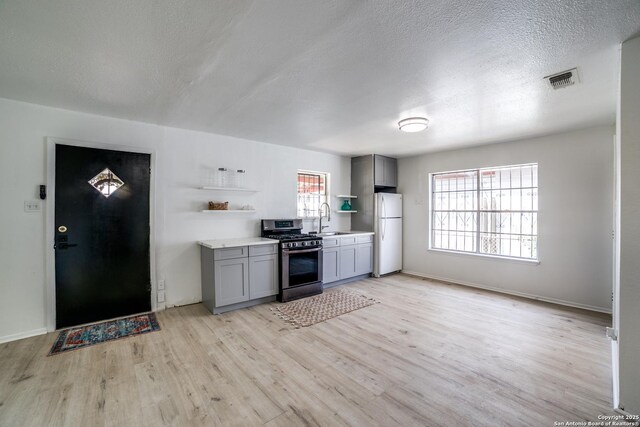 2114 S Trinity St, San Antonio, TX 78207 - kitchen featuring stainless steel gas range oven, freestanding refrigerator, gray cabinetry, a sink, and a textured ceiling