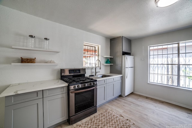 2114 S Trinity St, San Antonio, TX 78207 - kitchen featuring stainless steel gas range, freestanding refrigerator, open shelves, a sink, and gray cabinets
